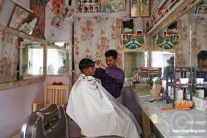 Young Indian barber in his barbershop cutting a boys hair, Jodhpur, Rajasthan, India