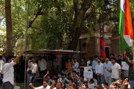 Delhi University students protesting at the Faculty of Arts with placards highlighting campus infrastructure and safety concerns.
