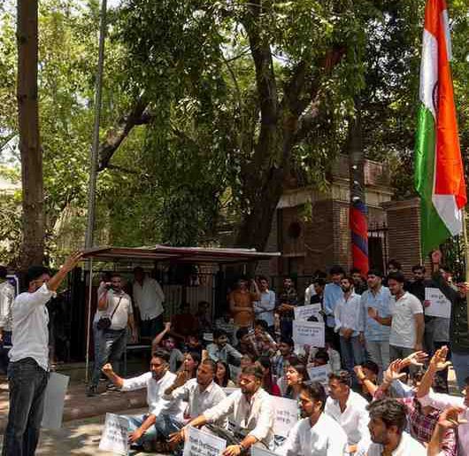Delhi University students protesting at the Faculty of Arts with placards highlighting campus infrastructure and safety concerns.