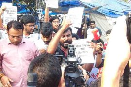 A group of students protesting in a crowded area with placards and media cameras during a demonstration related to NEET-UG 2026 concerns.