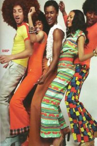 People in colourful 70s outfits pose together.