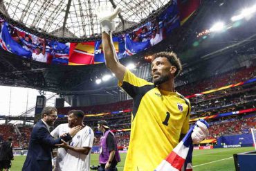 Cape Verde goalkeeper Vozinha waves to supporters after a 2026 FIFA World Cup match, holding the national flag inside a packed stadium.