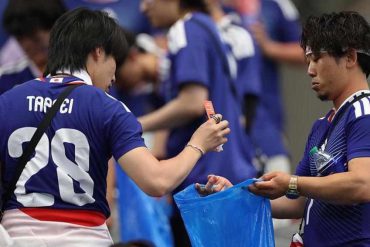 Japanese football fans sort litter into a blue garbage bag after a 2026 FIFA World Cup match.