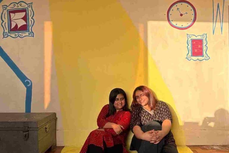 Sneha and Navya Misran at the library in Tughlakabad Village, against a wall painted by Kitaab Club and the children.